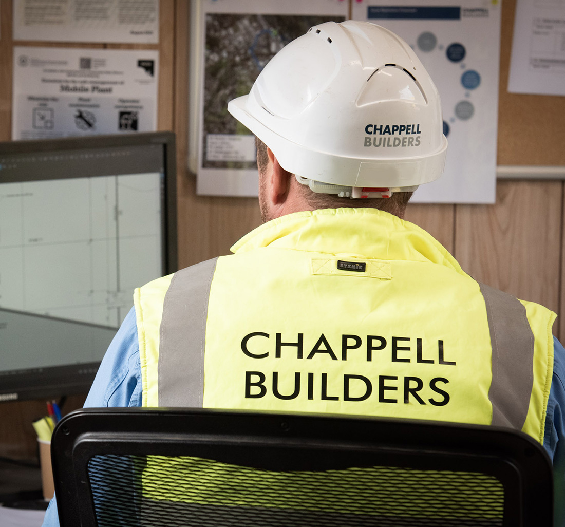 Worker in Chappell Builders Hi-Vis Vest and Hard Hat works on site computer